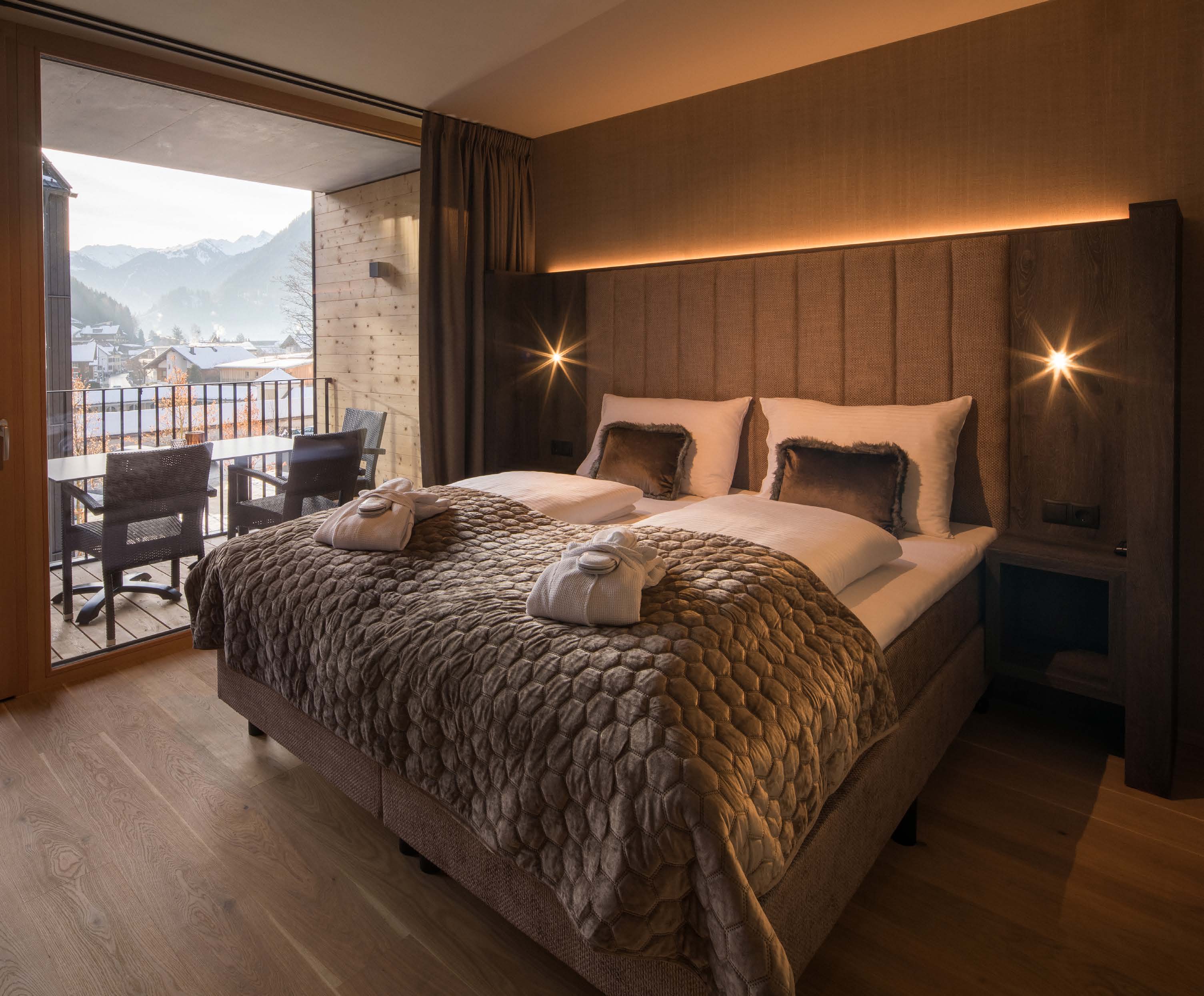 Schlafzimmer mit Boxspringbett und offener Balkontür mit Bergblick