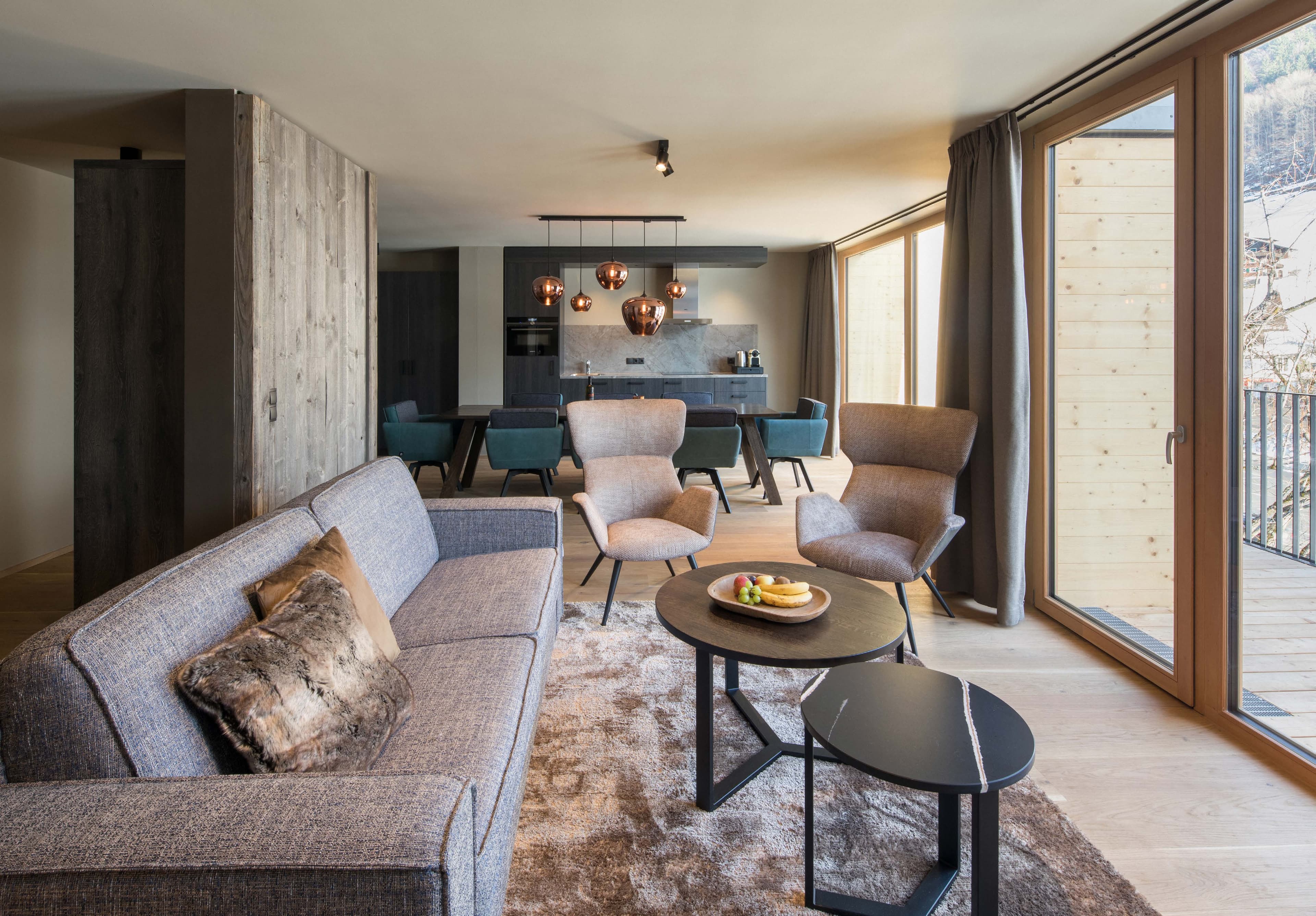 Wohnbereich eines Apartments mit Sofa, Sesseln, Essplatz und Balkontür